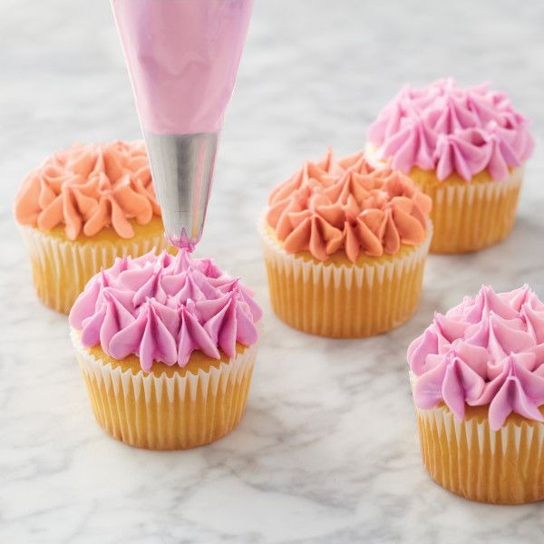 Cupcakes met roze en oranje druppelbloemen gespoten in botercrème, met een spuitzak met roze botercrème erboven.
