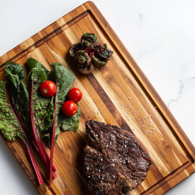 Teakhouten snijplank met sapgeul en handgrepen met een aangesneden steak, snijbiet en cherrytomaatjes