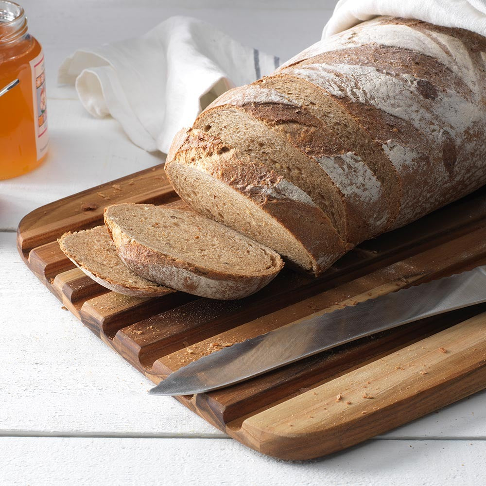 Vers brood in plakken gesneden op de Teakhaus Broodplank Essential, met een pot honing op de achtergrond.