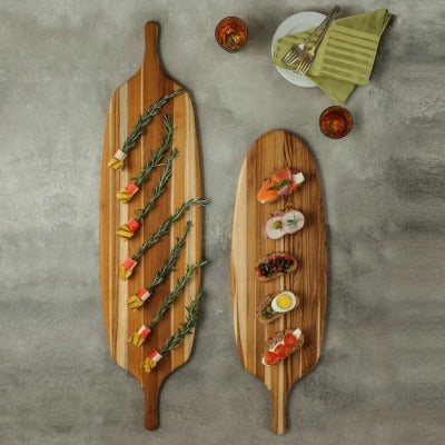 Twee Teakhaus Serveerplanken Canoe Paddle van bovenaf, belegd met hapjes aan prikkers en canapés voor bij de borrel.