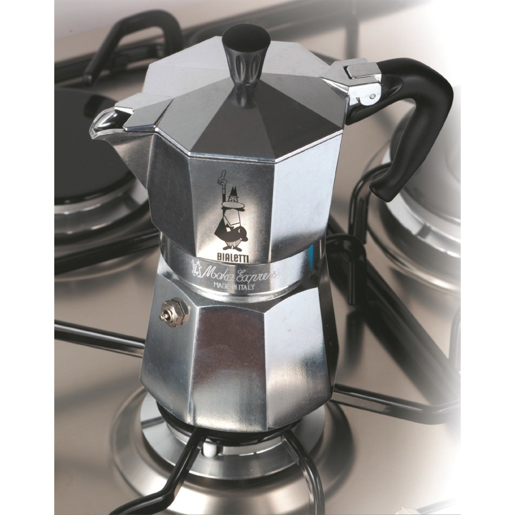 Grote zilveren Bialetti Moka Express percolator op een gaspit, met pannen op de achtergrond.