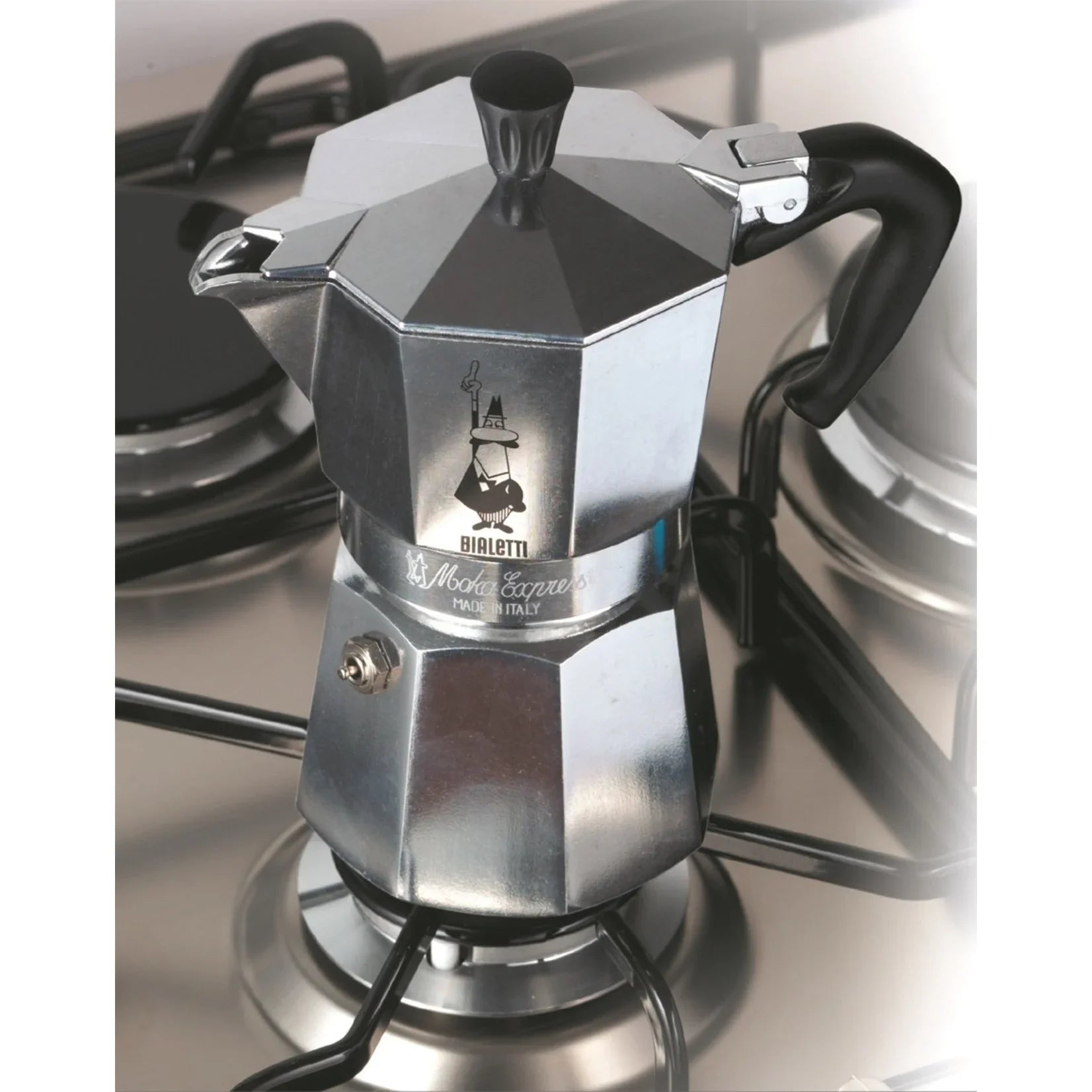 Zilveren Bialetti Moka Express percolator staand op een gaspit, met pannen op de achtergrond.