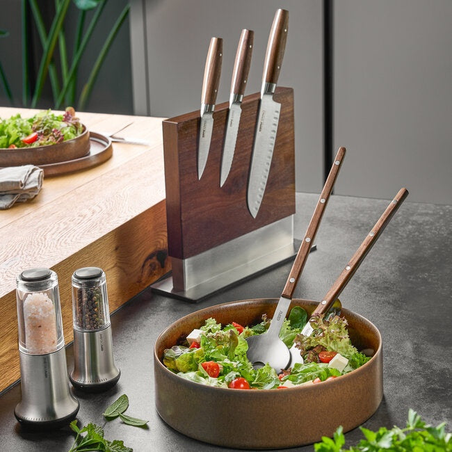 GEFU Saladebestek Filigo met de houten stelen rechtop in een kom verse salade, op een aanrecht met een messenblok en peper- en zoutmolen op de achtergrond