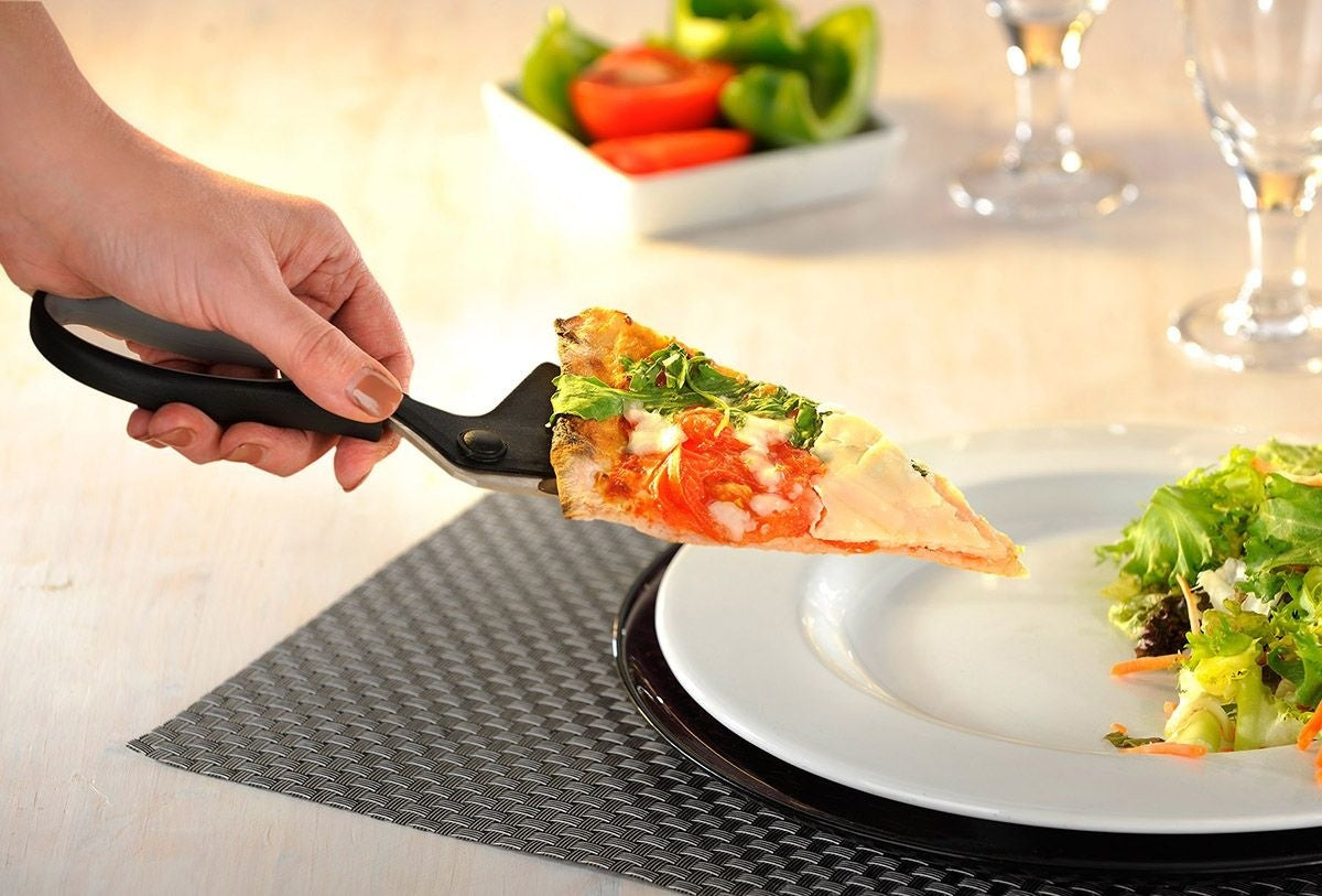 GEFU Pizzaschaar Pezzo, hand die met de ingebouwde spatel een pizzapunt van het bord tilt naast een schaaltje salade