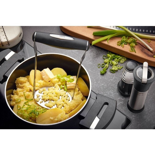 GEFU Aardappelstamper Timbra in een pan met gestampte aardappelen, met blokjes boter, gesneden bosui en een pepermolen op het aanrecht