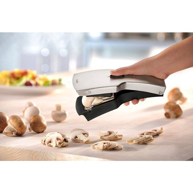 GEFU Snijder Tari, een hand snijdt met het apparaat verse champignons in plakjes op een houten tafel