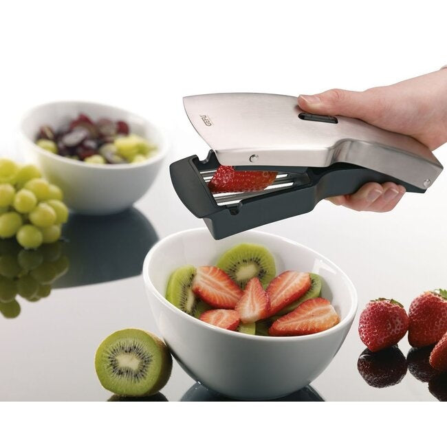 GEFU Snijder Tari, een hand snijdt een aardbei in plakjes boven een kom met kiwi, druiven en aardbeien