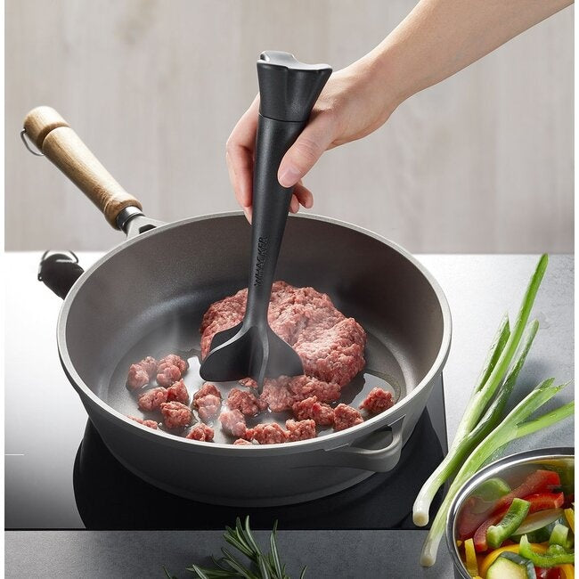 GEFU Universele Verdeler Whacker, hand die het apparaat gebruikt om gehakt te verkruimelen in een pan op het fornuis, met lente-ui en paprika ernaast