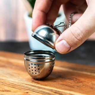 Westmark Teatime Ovaal Thee-ei, zilver, opengeklapt in de hand op een houten ondergrond