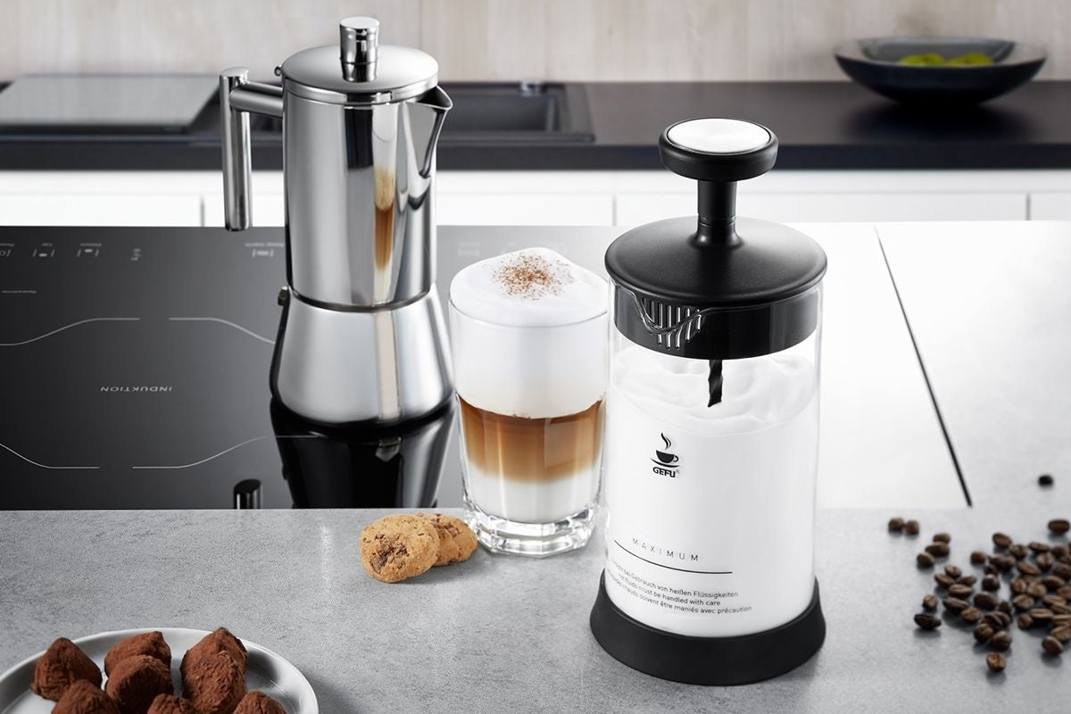 GEFU Melkopschuimer Antonio op het aanrecht naast een percolator en een glas latte macchiato, met een schaaltje koekjes