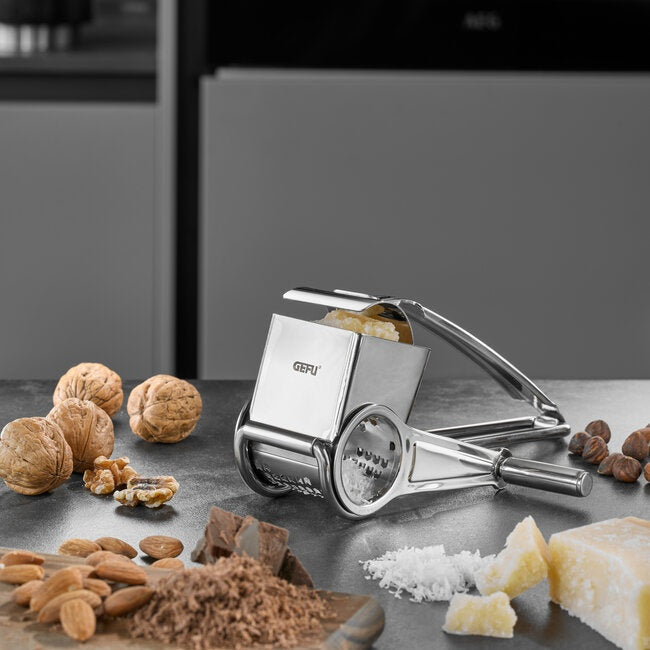 GEFU Kaasmolen Queso - RVS op een keukenblad tussen walnoten, amandelen, chocolade en blokjes kaas, die allemaal met de molen geraspt kunnen worden