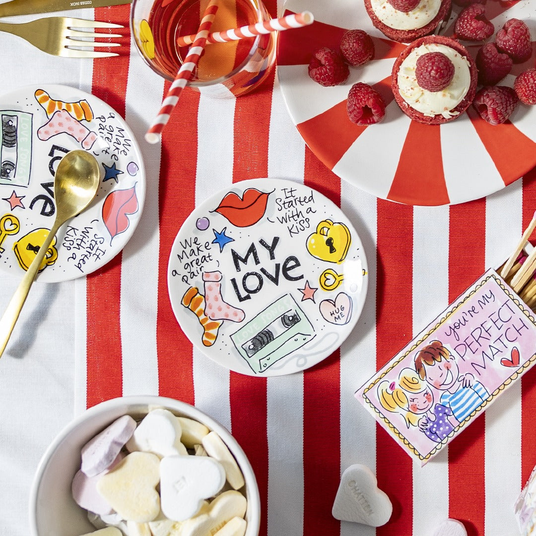 Blond Amsterdam Petit Four Love gebaksbord gedekt op een rood-wit gestreepte tafel, met gebakjes en bestek ernaast