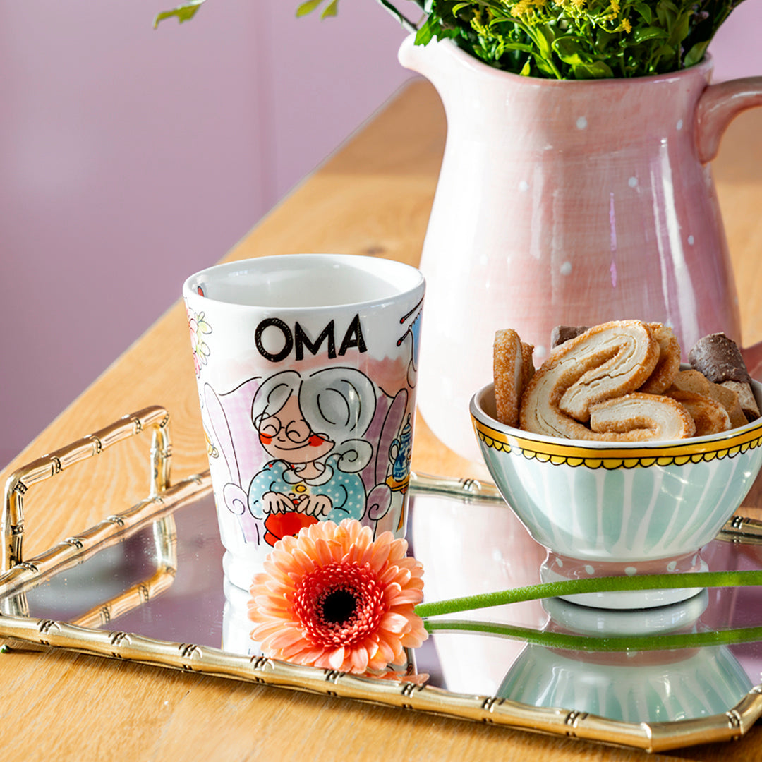 Blond Amsterdam Oma-mok op een gouden dienblad met koekjesschaaltje en roze gerbera