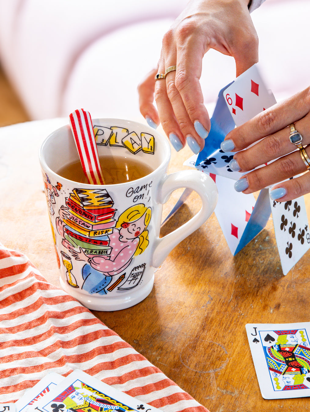 Blond Amsterdam Game on mok met thee op houten tafel, handen met speelkaarten ernaast