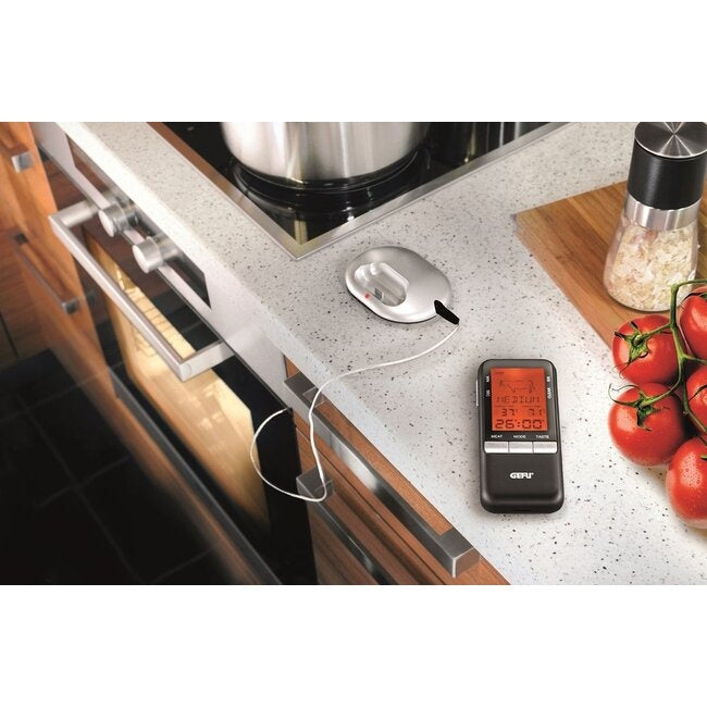 GEFU Digitale Thermometer Handi op een keukenblad naast het fornuis, met de kabel van de meetpen naar het kookvak en de zwarte display-eenheid op het aanrecht tussen tomaten aan de tros