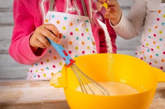 Kind in gekleurde sterrenschort klopt eieren en suiker met de Kuhn Rikon Kindergarde in een gele mengkom.