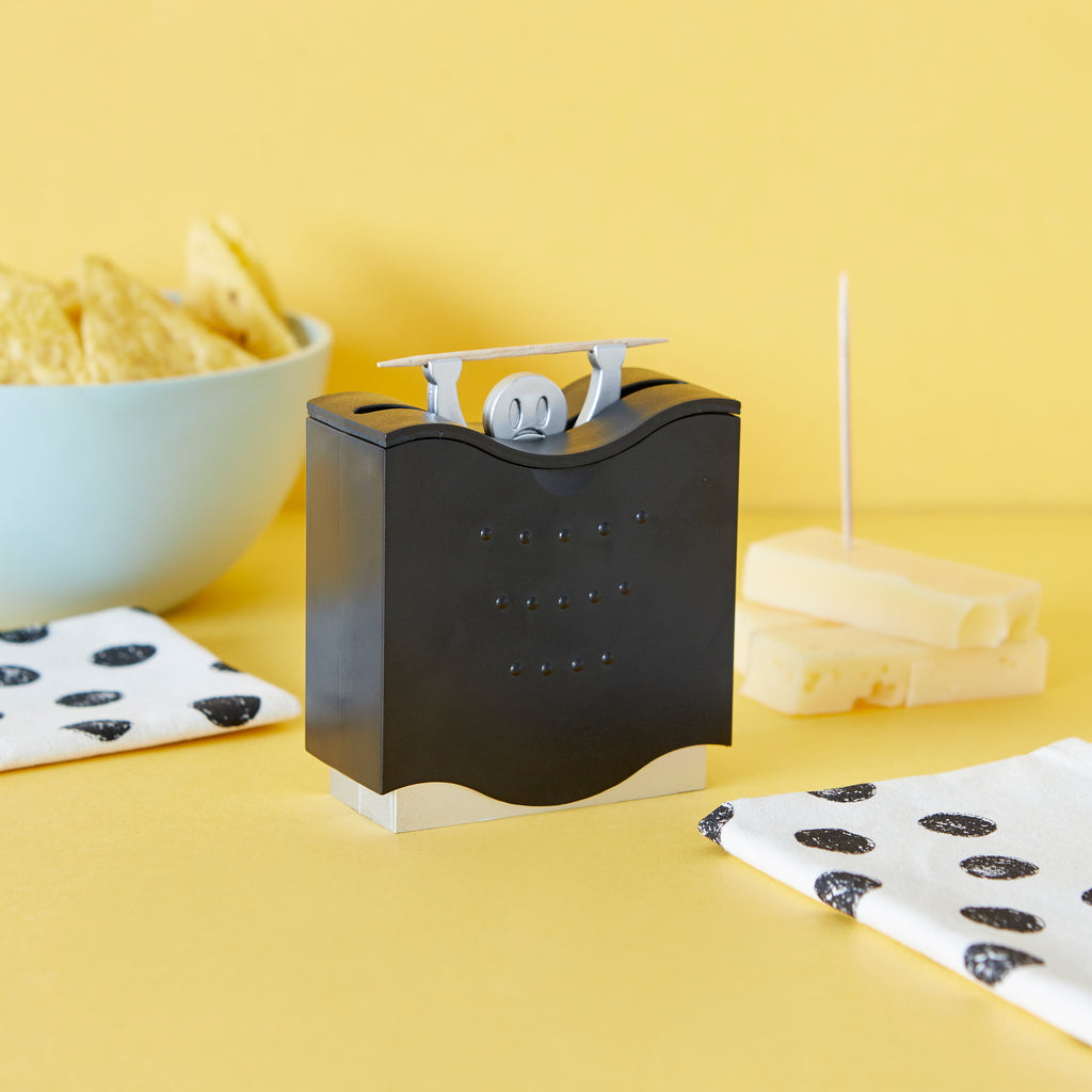 Balvi Pick a Boo dispenser op gele achtergrond naast chips en kaasstengels
