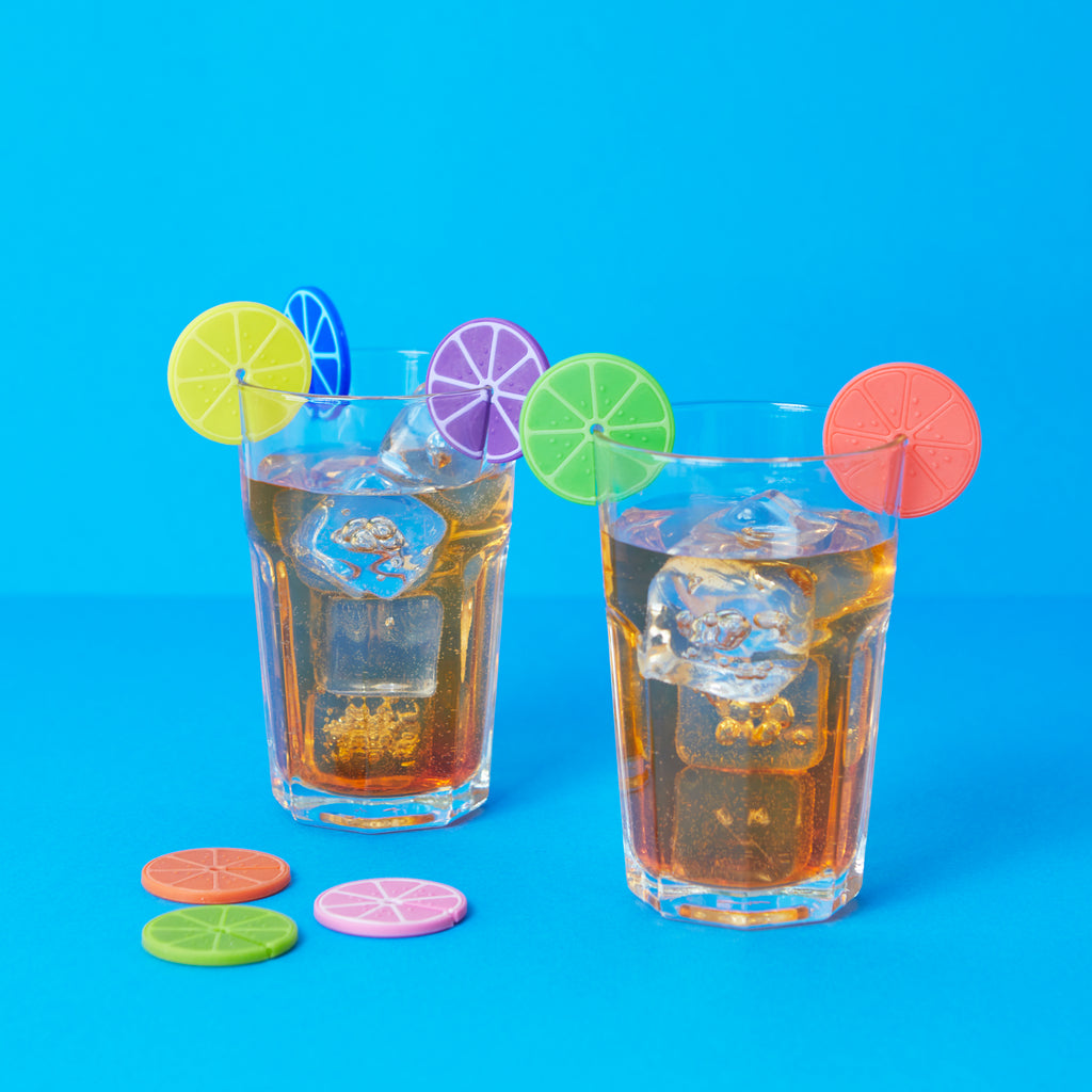 Twee glazen frisdrank met ijs en Balvi citrus-glasmarkers tegen blauwe achtergrond
