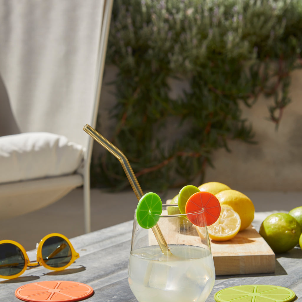 Glas water met gouden rietje en Balvi citrus-markers op een buitentafel met citroenen en limoenen