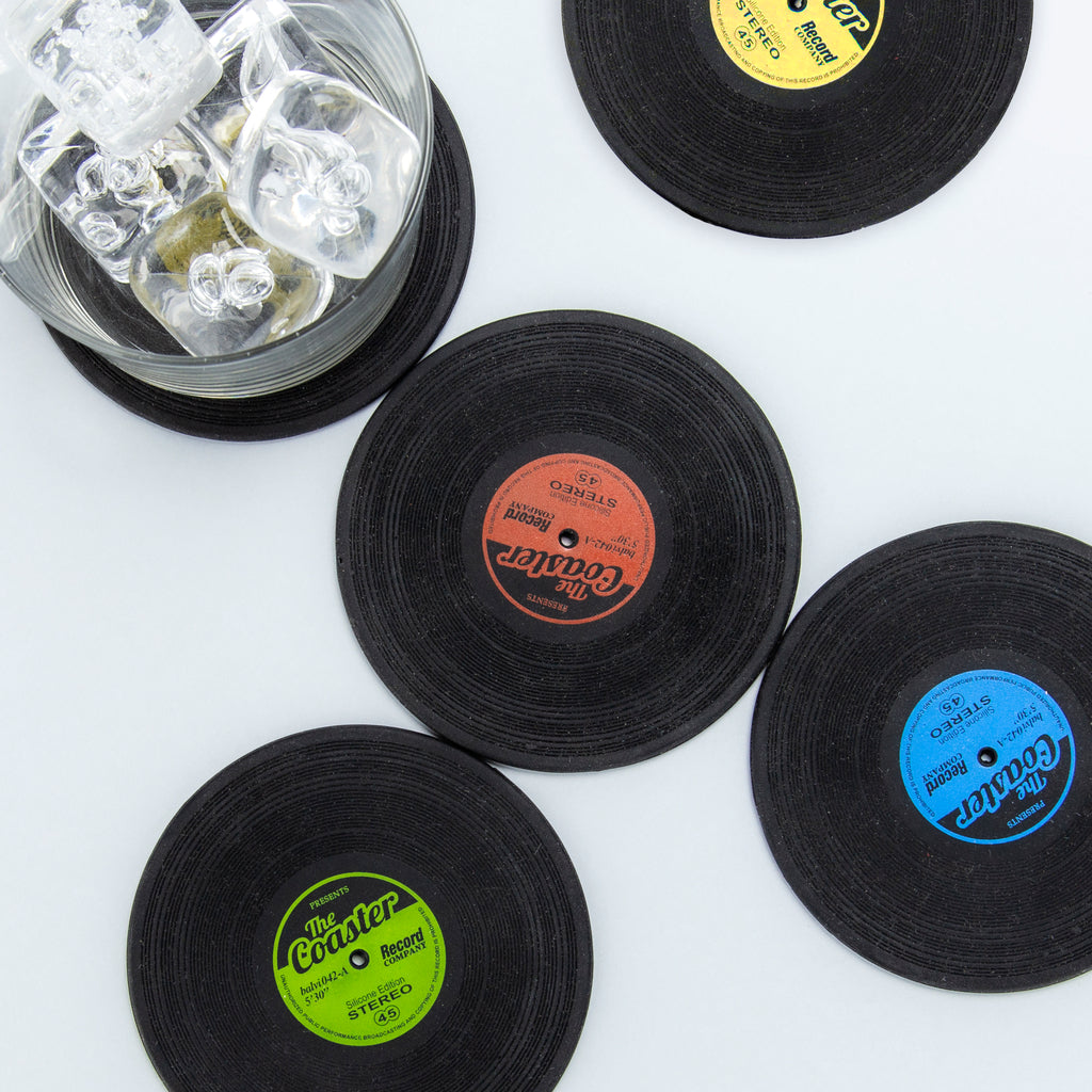 Balvi Onderzetters The Coaster - 4 stuks, bovenaanzicht van zwarte vinylplaat-onderzetters met geel, rood, groen en blauw label en een glas met ijs