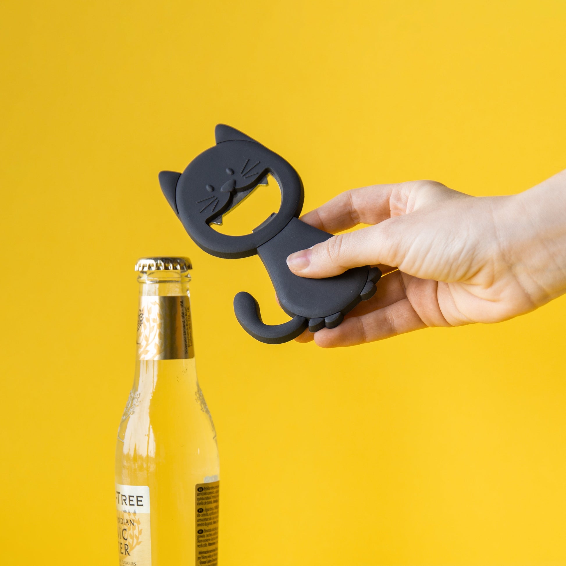 Balvi Flesopener Katy, op gele achtergrond, vastgehouden in de hand terwijl een bierflesje wordt geopend