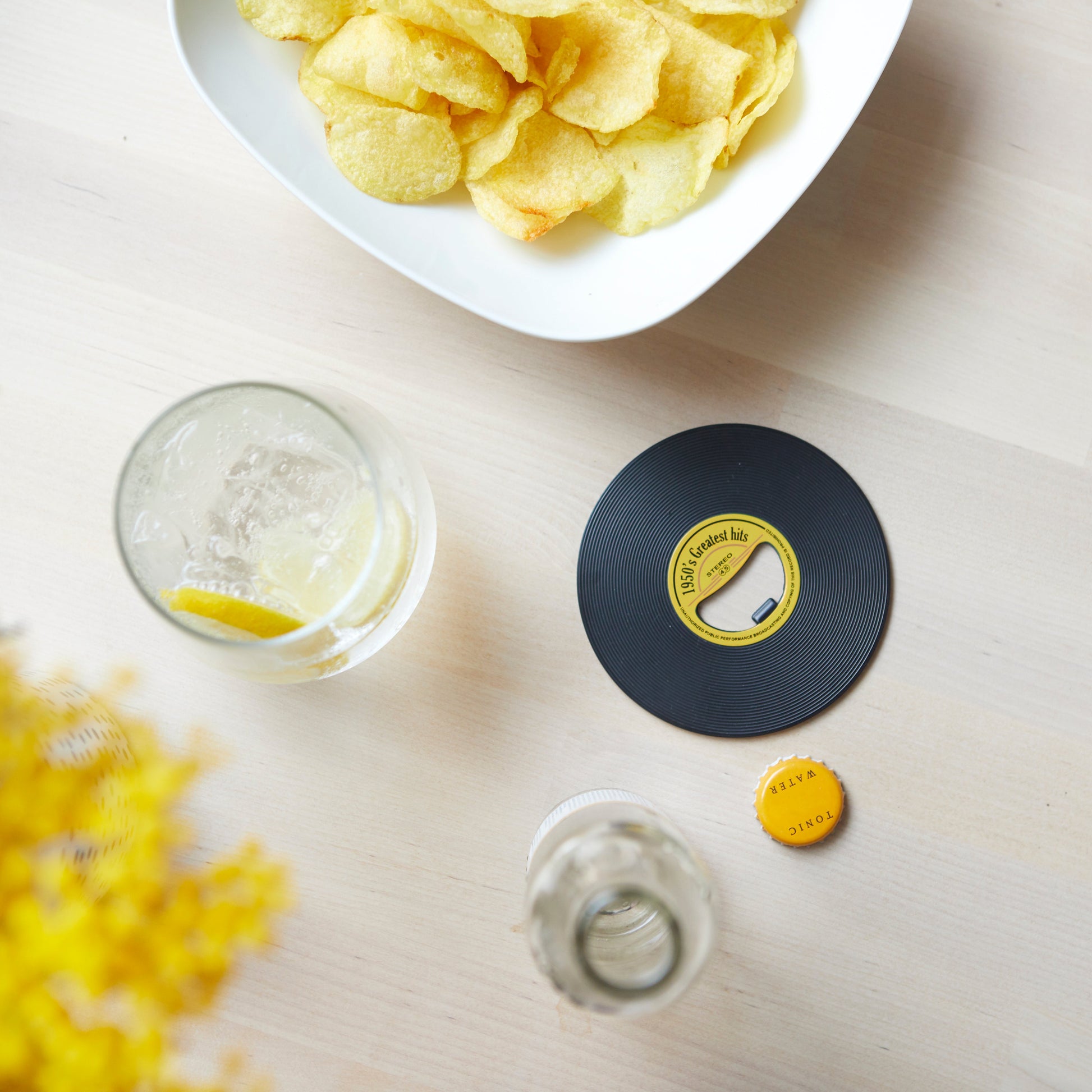 Balvi Flesopener Greatest Hits, op een houten tafel met chips en een drankje