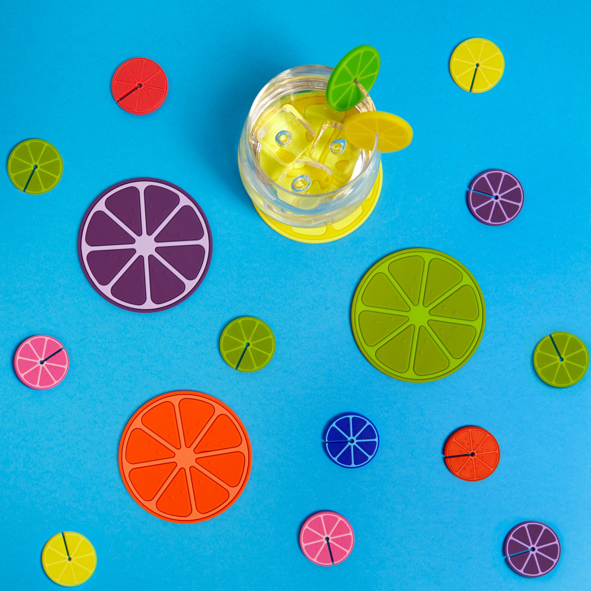 Balvi Onderzetters Fruit Party - 4 stuks, op blauwe achtergrond met verspreide onderzetters en een drankje met munt