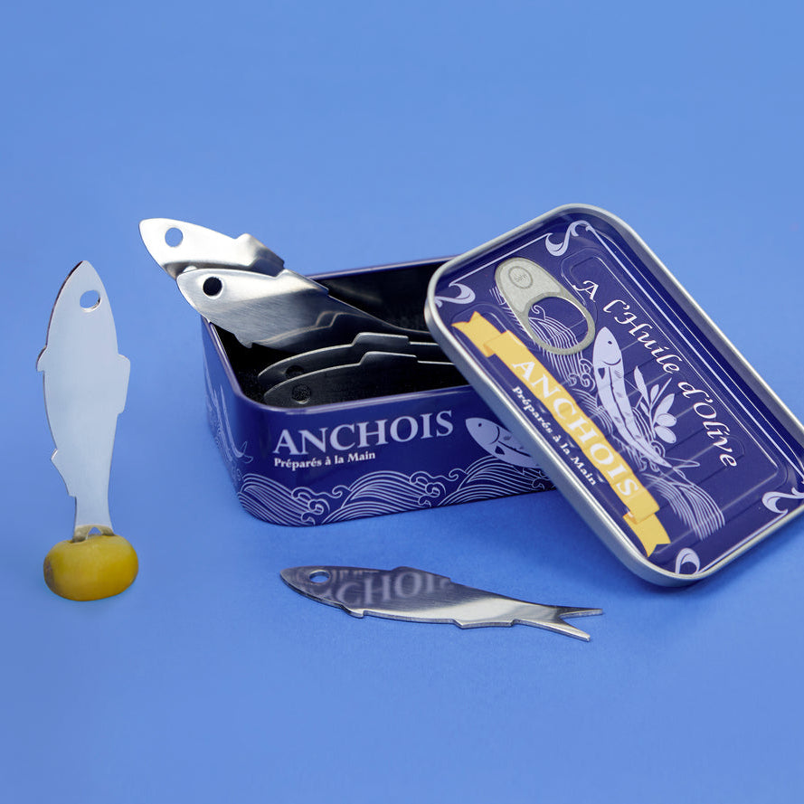 Open donkerblauw blik met ansjovisvorkjes en een vorkje met olijf, tegen een blauwe achtergrond