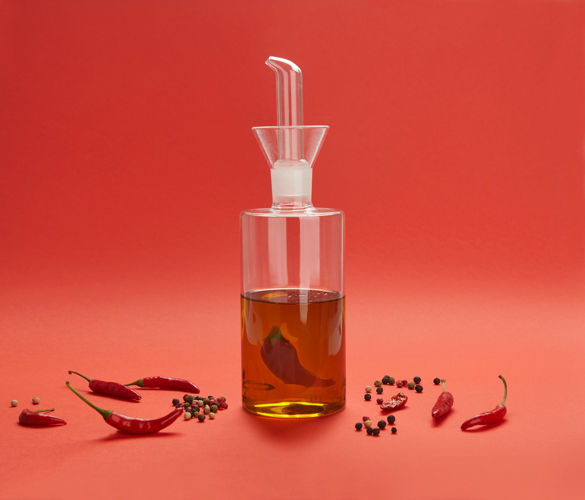 Balvi Olieschenker Chili - 350 ml, op rode achtergrond met chilipepers, gevuld met olie