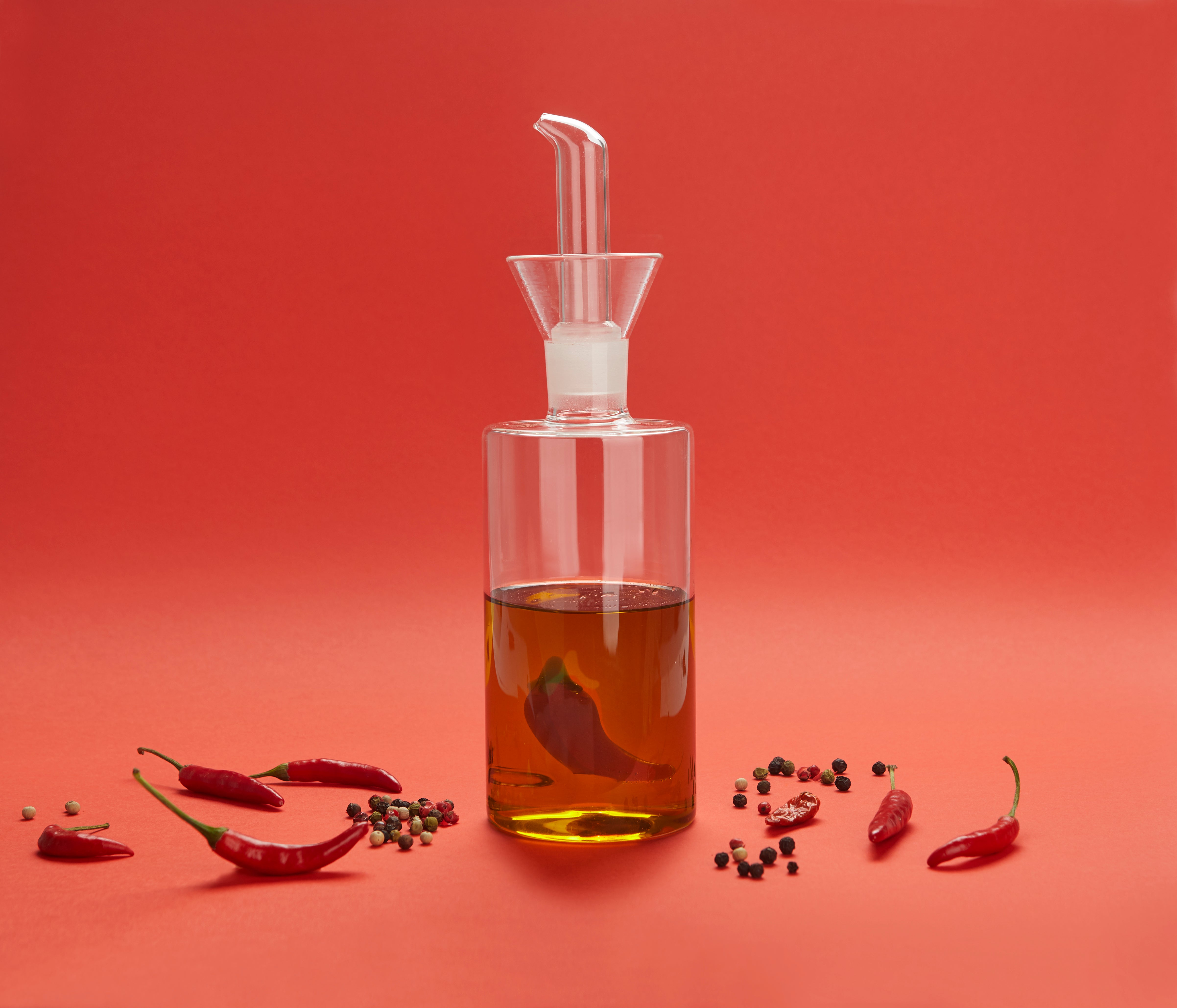 Balvi Olieschenker Chili - 350 ml, op rode achtergrond met chilipepers, gevuld met olie
