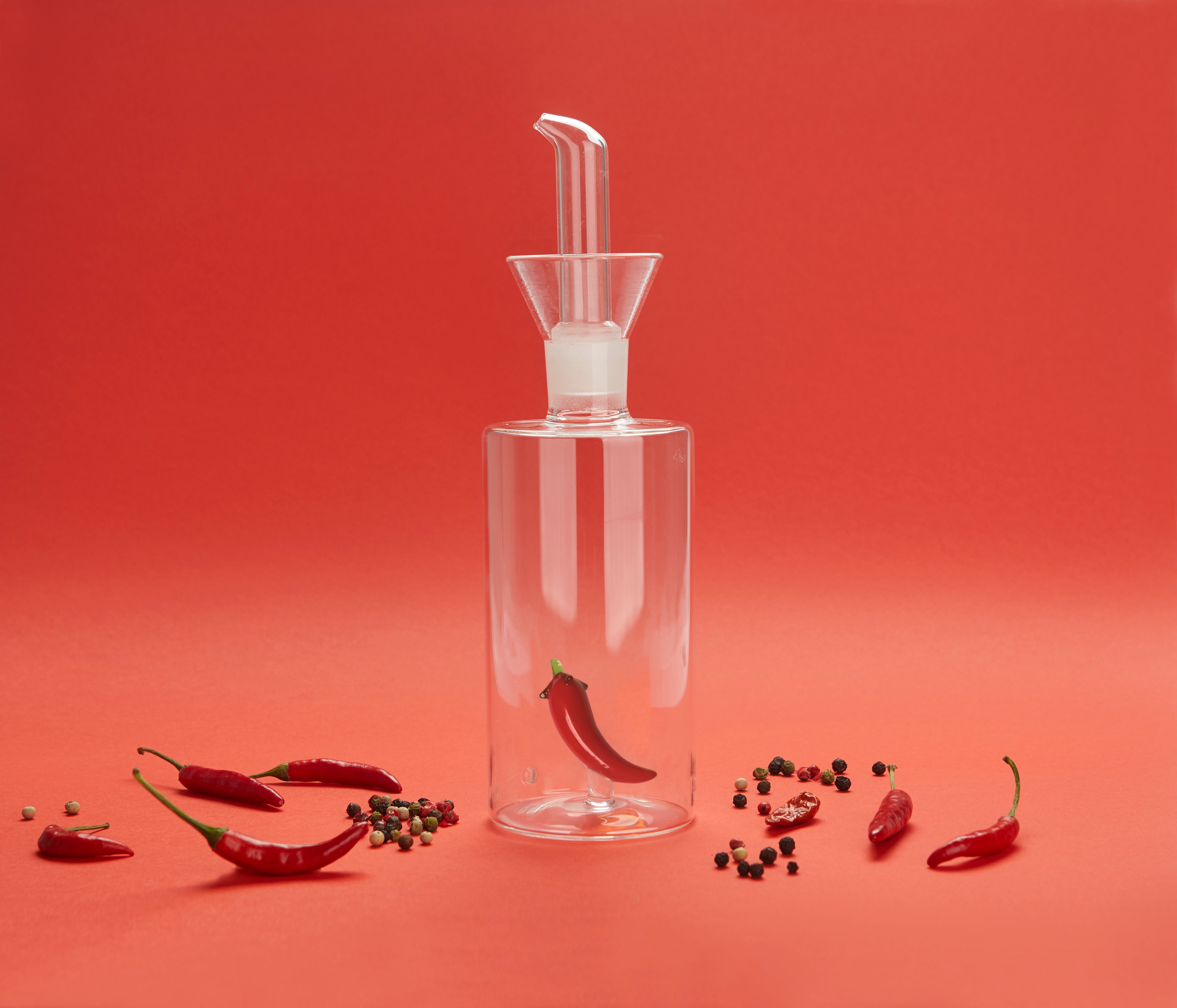 Balvi Olieschenker Chili - 350 ml, op rode achtergrond met chilipepers