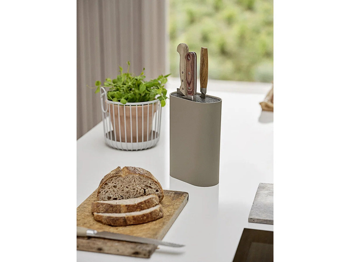 Taupe messenblok met drie messen met houten handgrepen op een wit aanrecht, met brood op een snijplank