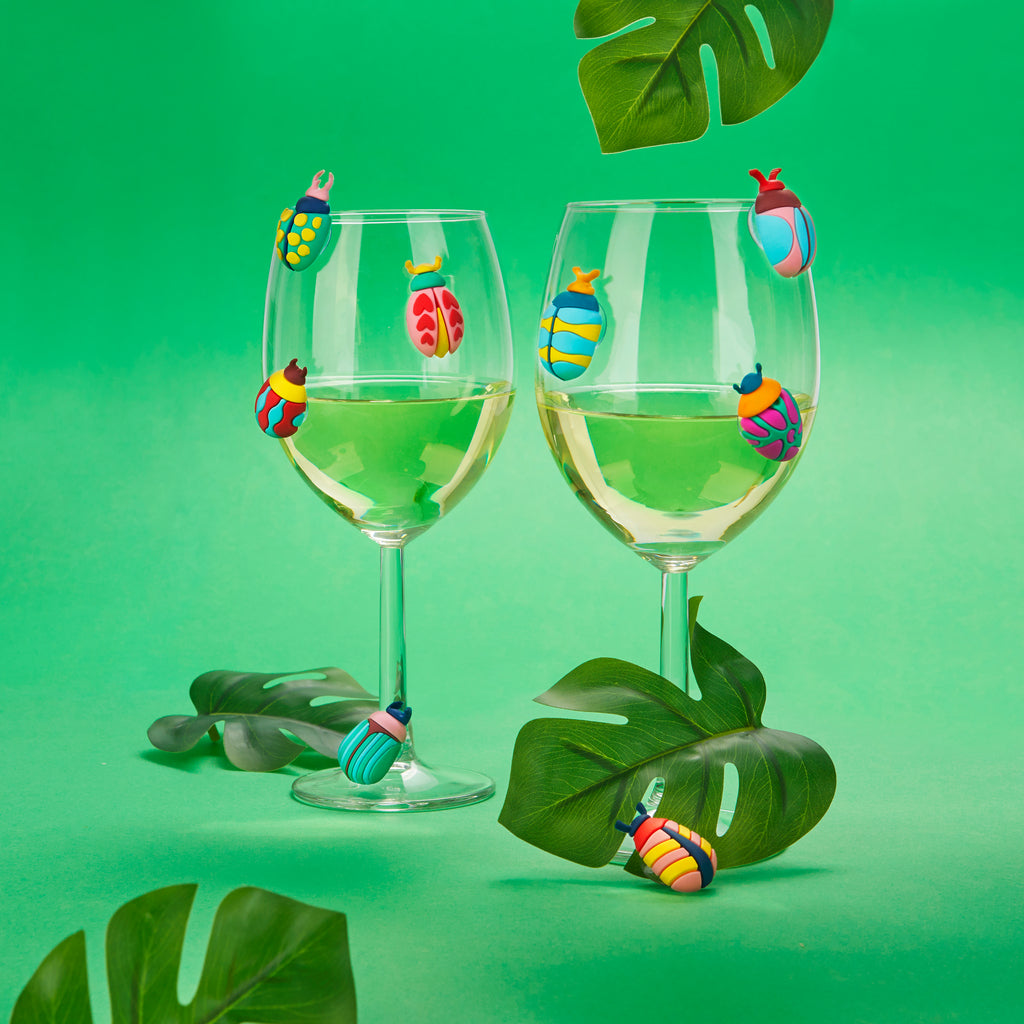 Twee wijnglazen met kevermarkers tegen een groene achtergrond met monsterabladeren