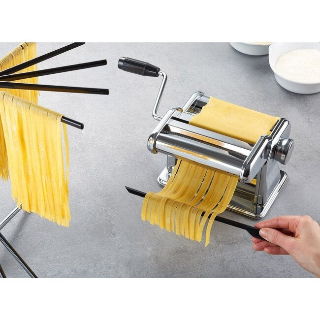 GEFU Pastadroger Diverso - Groot met pastalinten aan de armen, naast een pastamachine waar met de hand aan gedraaid wordt