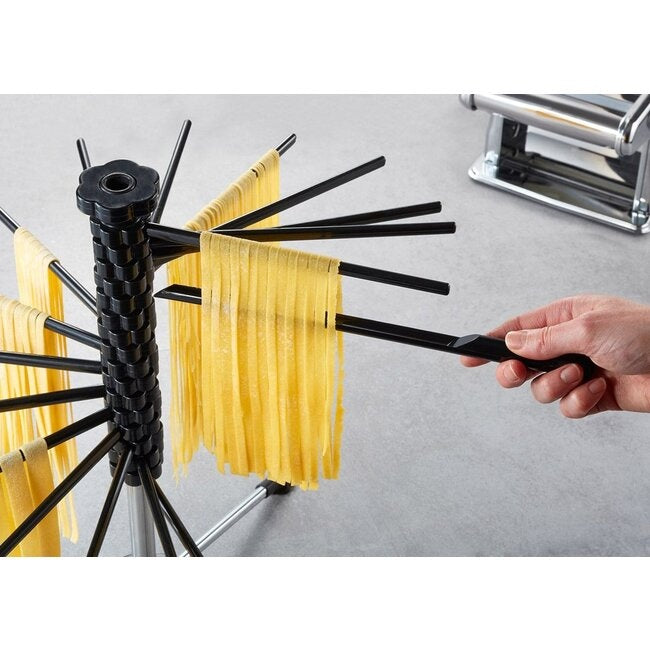 GEFU Pastadroger Diverso - Groot, close-up van een hand die met een tang een pastalint van de machine naar de droger brengt