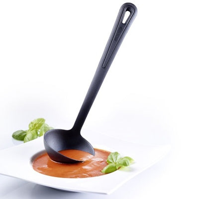 Westmark Gentle Plus Soeplepel, zwart, lepel rechtop in een bord tomatensoep met basilicumblaadjes