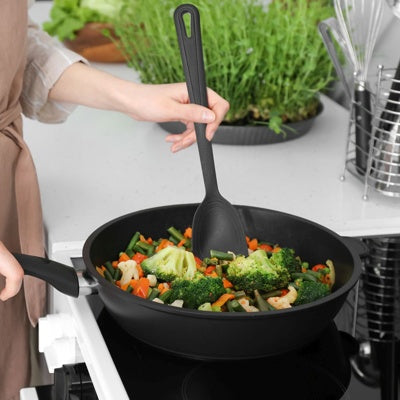Westmark Gentle Opscheplepel, zwart, in gebruik boven een wokpan met broccoli en wortel op het fornuis
