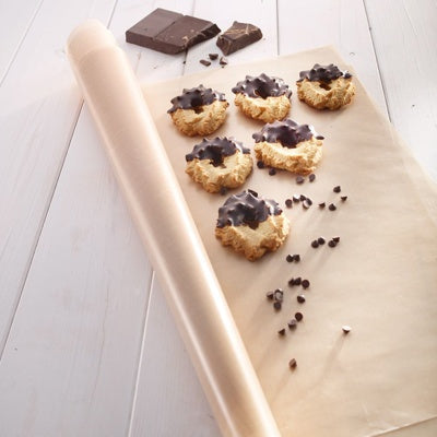 Westmark Herbruikbare Bakfolie, transparant, opgerold naast bakpapier met koekjes en stukjes chocolade