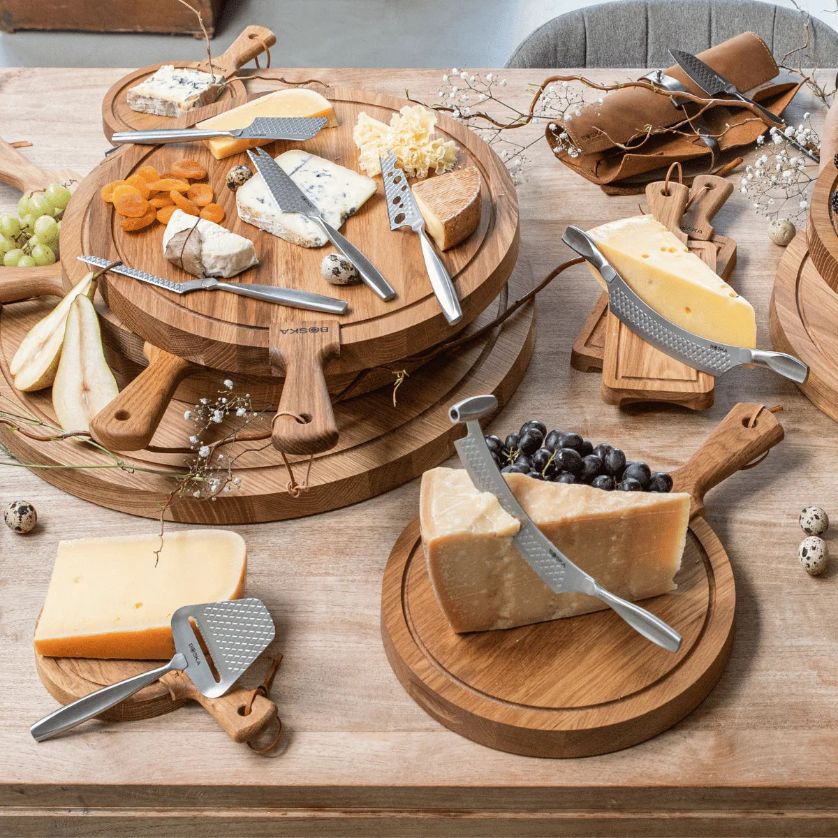 Boska Monaco+ Comté Mes Nr. 7 op een tafel met meerdere kaasplanken, fruit en andere Boska messen