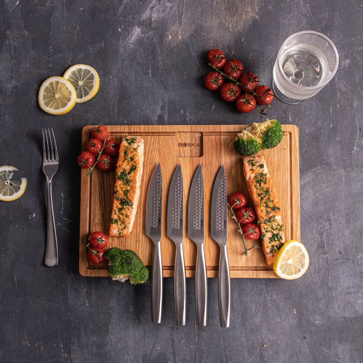 Boska Monaco+ Steakmessen 4-delig naast zalmfilets, tomaatjes en citroen op een plank