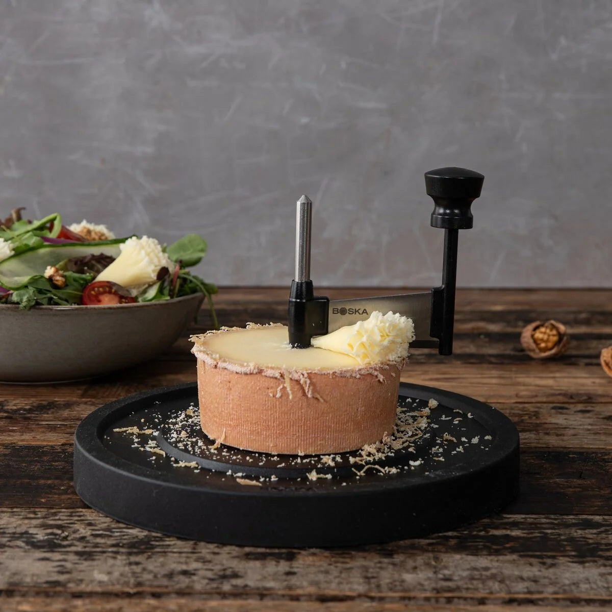 Boska Milano Kaaskruller met kaaswiel op een houten tafel, salade op de achtergrond