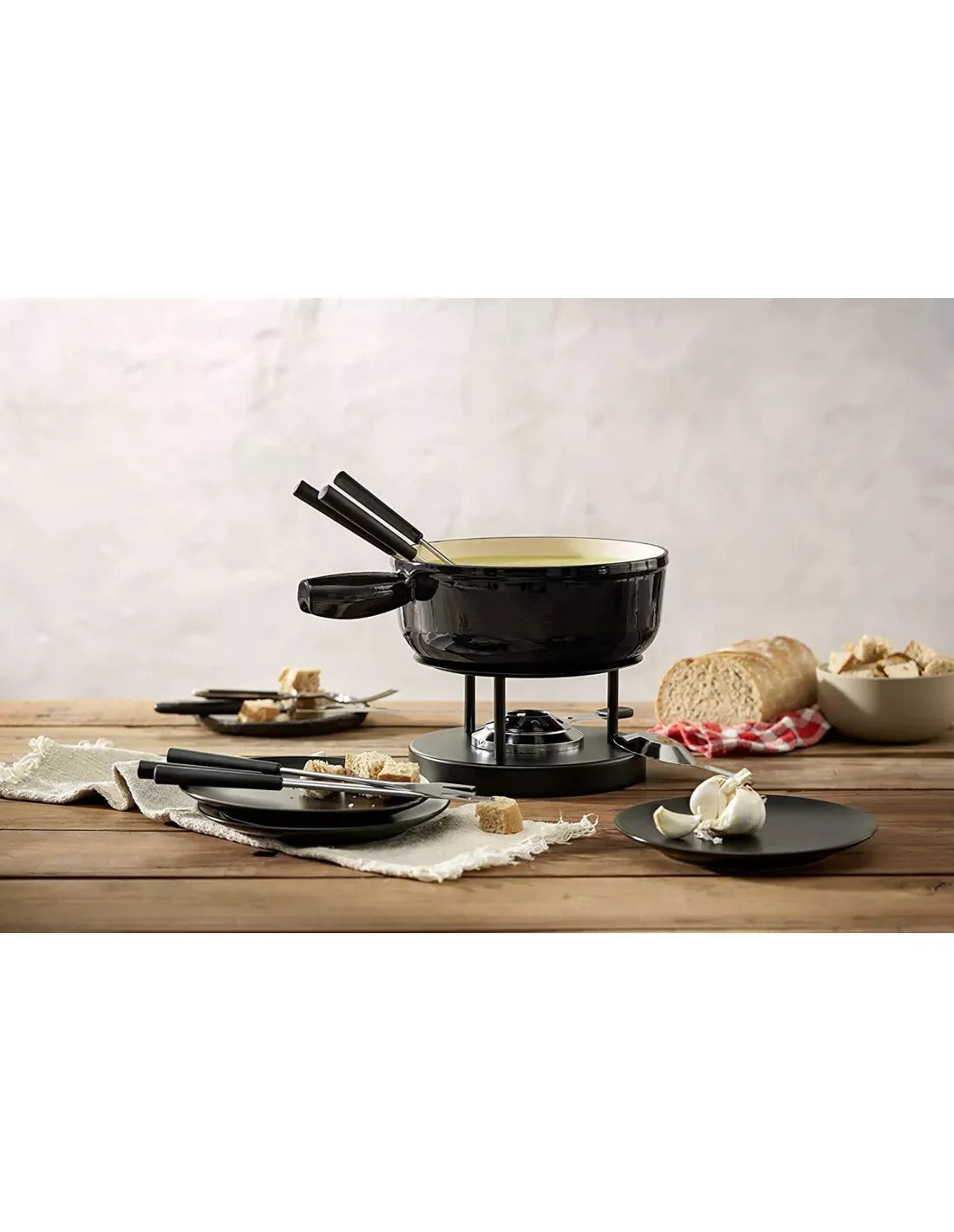 Tafelscène met zwarte Caquelon op rechaud, dampende kaasfondue, drie fonduevorken met zwart handvat, brood en een geruit theedoekje op een houten tafel.
