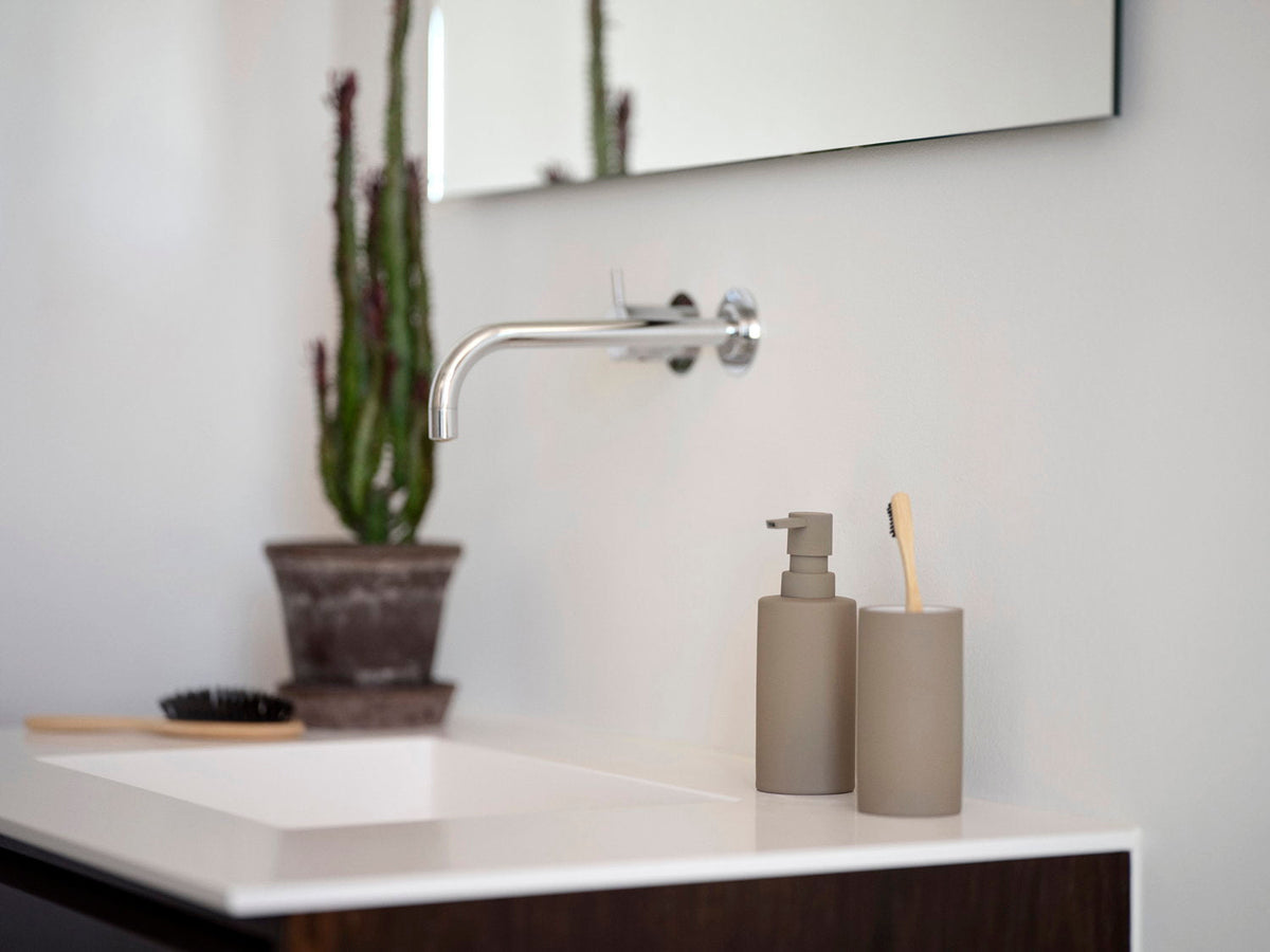 Taupe Zone Denmark Solo zeepdispenser op een badkamerblad naast een cactus, met een haarborstel ernaast