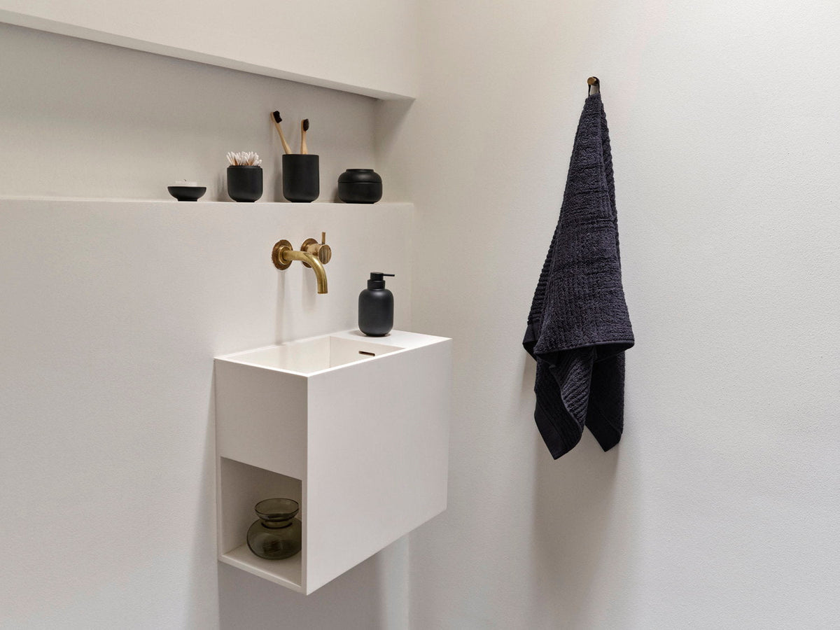 Badkamerplank met Zone Denmark Sensu zeepdispenser en accessoires, wastafel met gouden kraan eronder