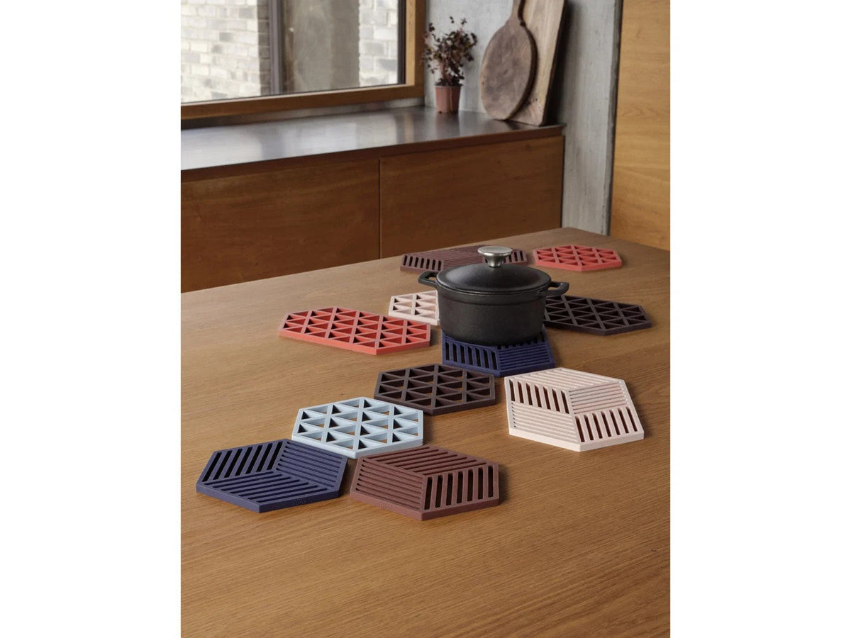 Houten tafel met zwarte gietijzeren pan op een blauwe onderzetter, omringd door onderzetters in roodbruin, roze en lichtblauw