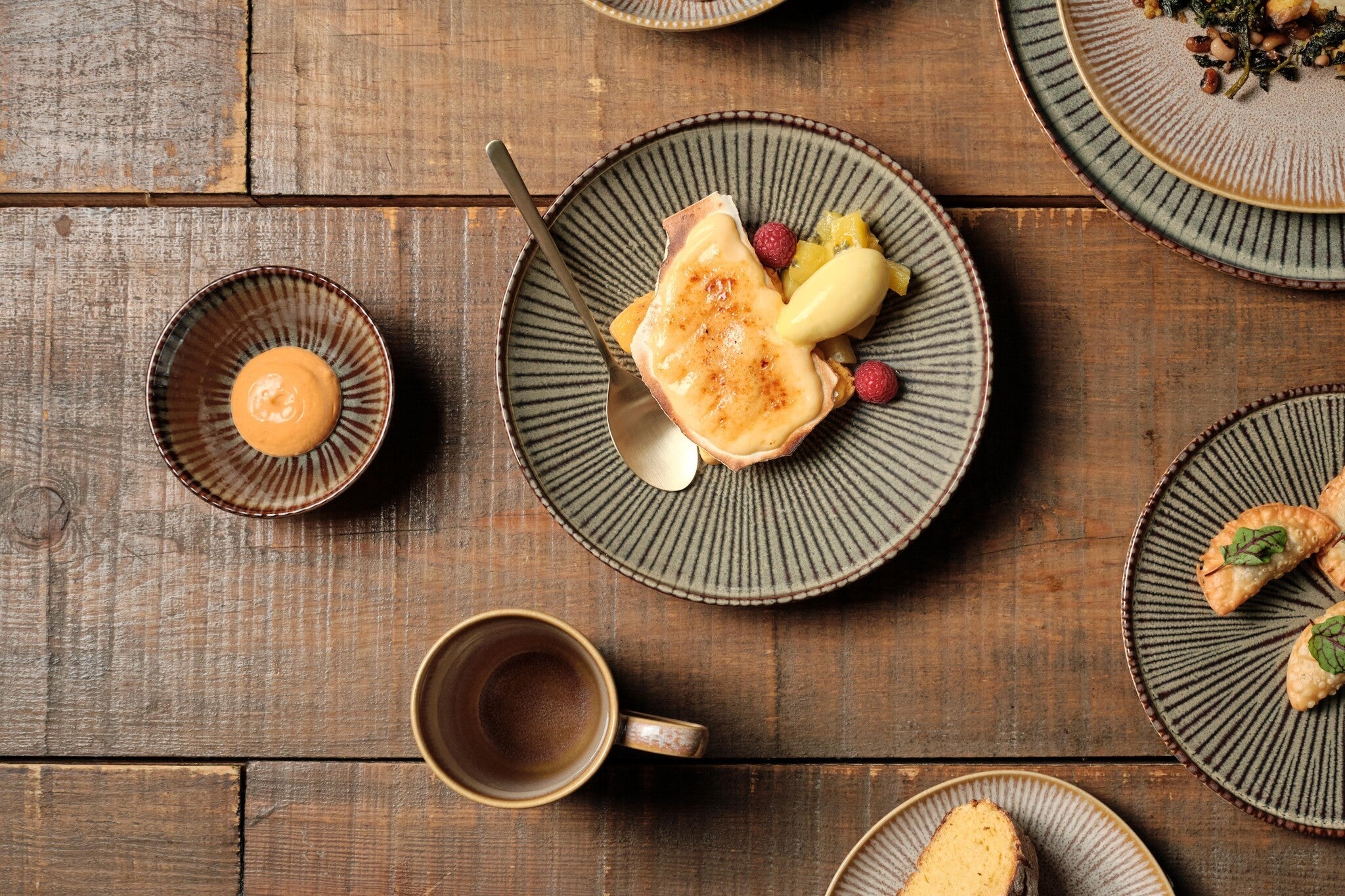 Casa Alegre Shangri-la Ontbijtbord Donker - 22 cm, met een dessert van brulée-crème, ananas en frambozen, naast een schaaltje saus en andere gerechten op tafel