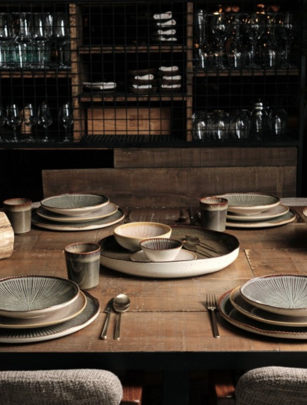 Gedekte houten tafel met Shangri-la servies in licht en donker: dinerborden met bijpassende bekers, een ronde donkere schaal met hapjes en een grote ovale serveerschaal met gebraden vlees en aardappelen