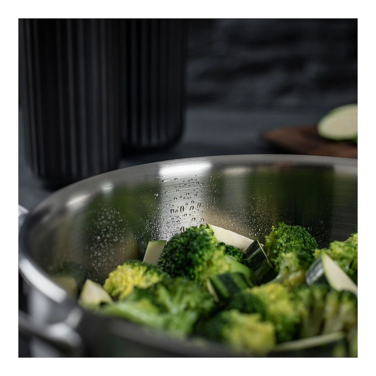 Binnenkant van de chefpan 24 cm gevuld met broccoli en courgette, met waterdruppels op de gepolijste rand.