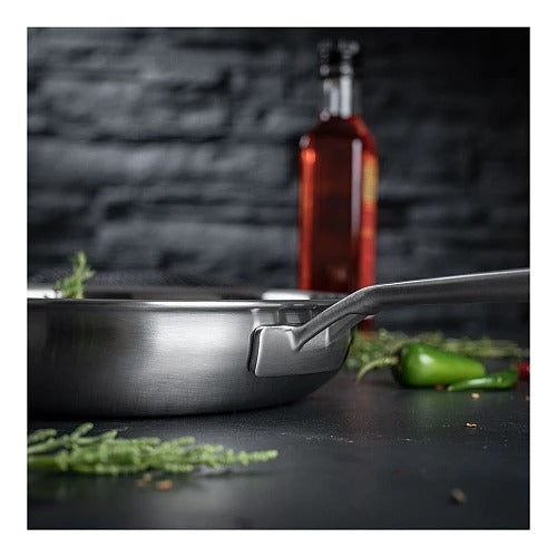 Detailfoto van de klinknagelverbinding aan het handvat van de Culinary 5-Ply koekenpan 24 cm, met een vervaagde groene peper op de achtergrond.