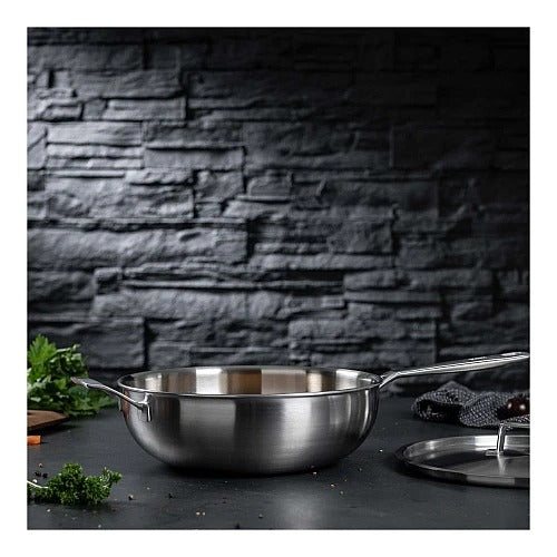 De Culinary 5-Ply wok met deksel 28 cm op een donker aanrecht, met de deksel losstaand ernaast en verse kruiden en cherrytomaten op de voorgrond.